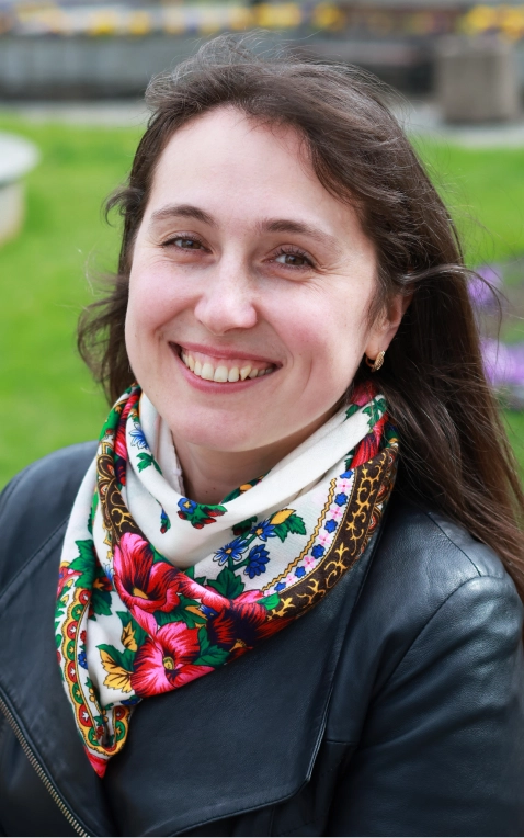 Natural Pharmaceuticals OmegaMarine Junior+™ Uśmiechnięta kobieta z długimi brązowymi włosami, ubrana w czarną skórzaną kurtkę i kolorową chustę w kwiaty