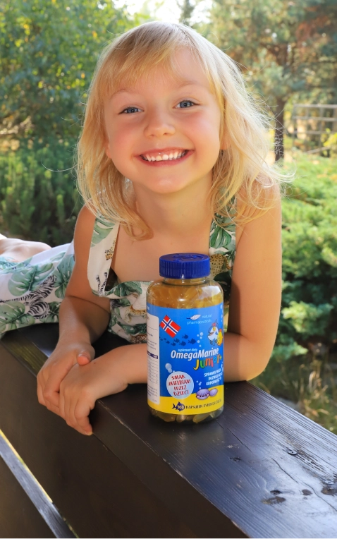 Natural Pharmaceuticals OmegaMarine Junior+™ Radosna dziewczynka prezentująca suplement OmegaMarine Junior w ogrodzie